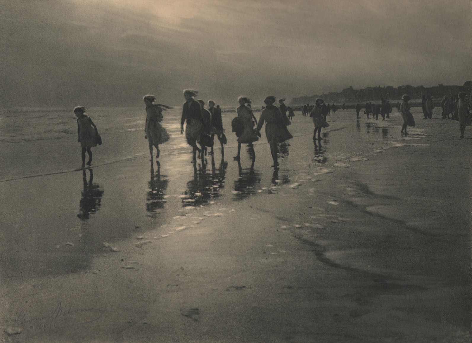 21. L&eacute;onard Misonne, La brise, 1926. A group of girls walk along the beach with bare feet in the water. Gray/green-toned print.