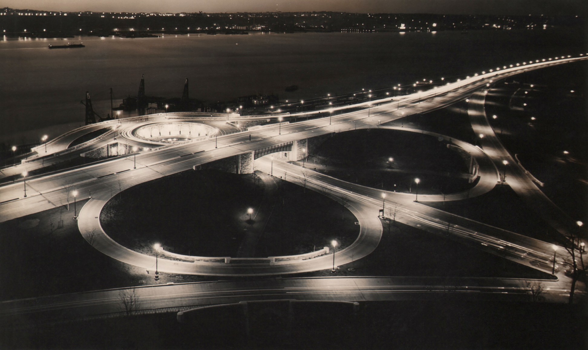 Paul J. Woolf, 86th Street Clover Leaf at Night, ​c. 1935. Night time view of riverside street with circular on- and off-ramps.