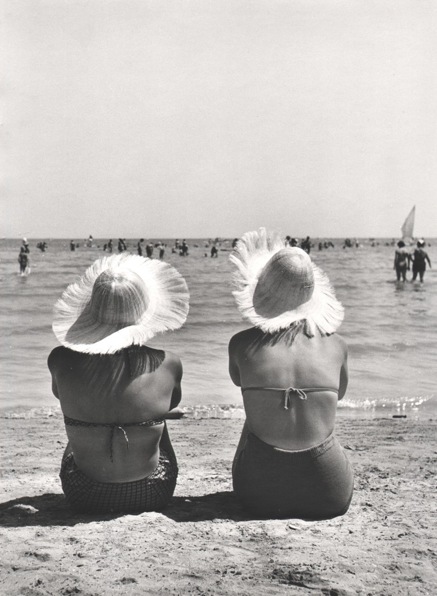 Nino Migliori, Bathing Beauties, 1954. Two woman sitting on the beach in straw hats, photographed from behind.