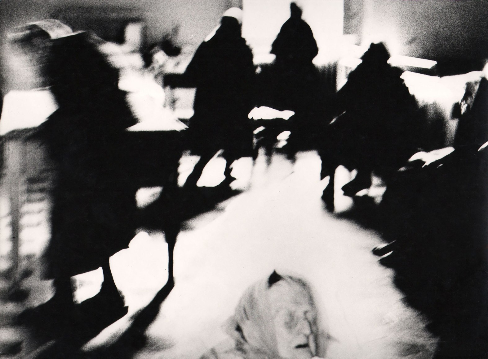 33. Mario Giacomelli, Verr&agrave; la morte e avr&agrave; i tuoi occhi, 1966&ndash;1968. High contrast image, blurred with motion. The head of an old woman with eyes closed in the bottom center of the frame, surrounded by dark silhouettes moving around the room.