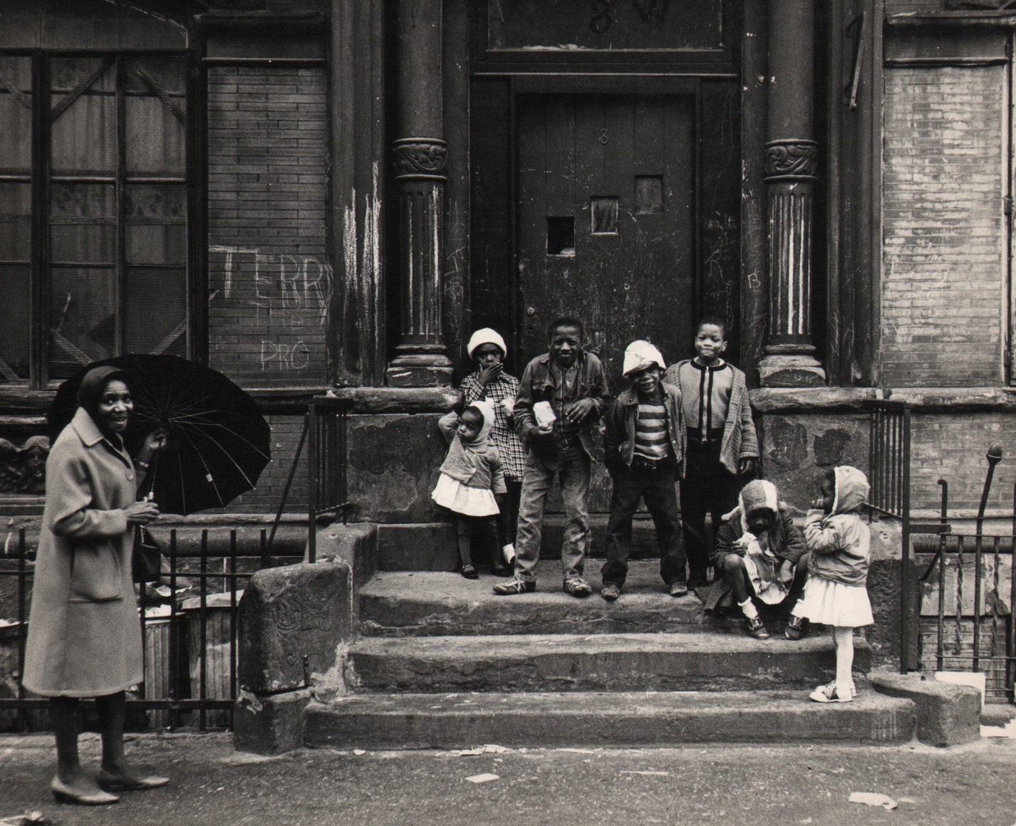 25. Beuford Smith, Harlem Children, Easter Sunday, ​1965. Seven children lined up on a stoop; a smiling woman holding an umbrella stands in the lower left of the frame.