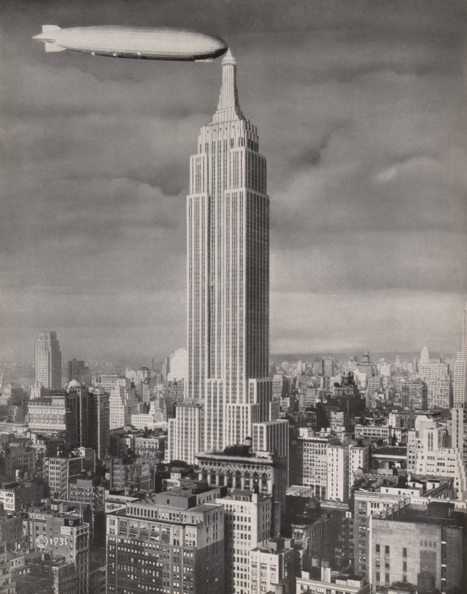 18. Panorama Studio, Empire State Building &amp; Dirigible &quot;Los Angeles,&quot; ​1931. Head-on view of the Empire State Building against a cloudy sky. The nose of a dirigible meets the building's tower on the left.