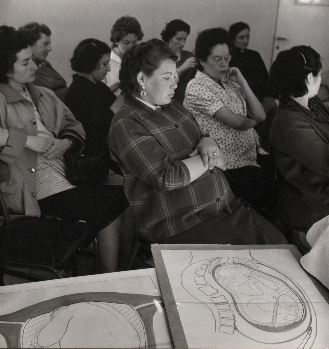 49. Janine Ni&eacute;pce, Untitled, c. 1960. A group of seated women with crossed arms. Anatomical pregnancy diagrams are on a table in the foreground.