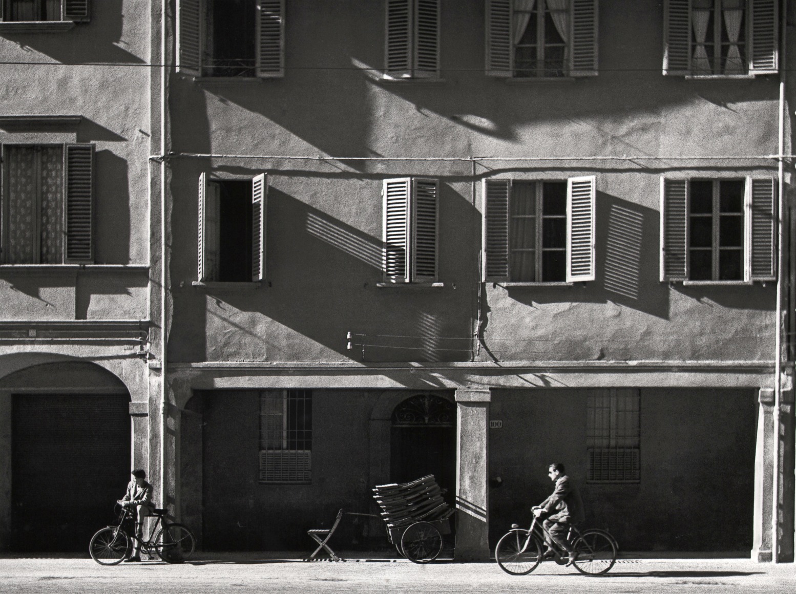Nino Migliori, The house opposite, 1954. Two men ride bicycles in front of an apartment building