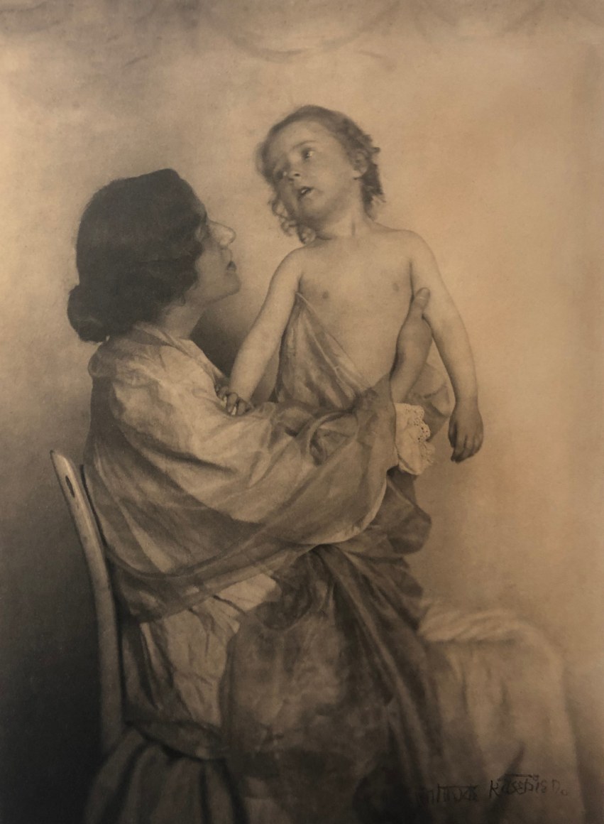 02. Gertrude K&auml;sebier, Adoration, ​1897. A seated woman in profile holds a small child upright on her lap.