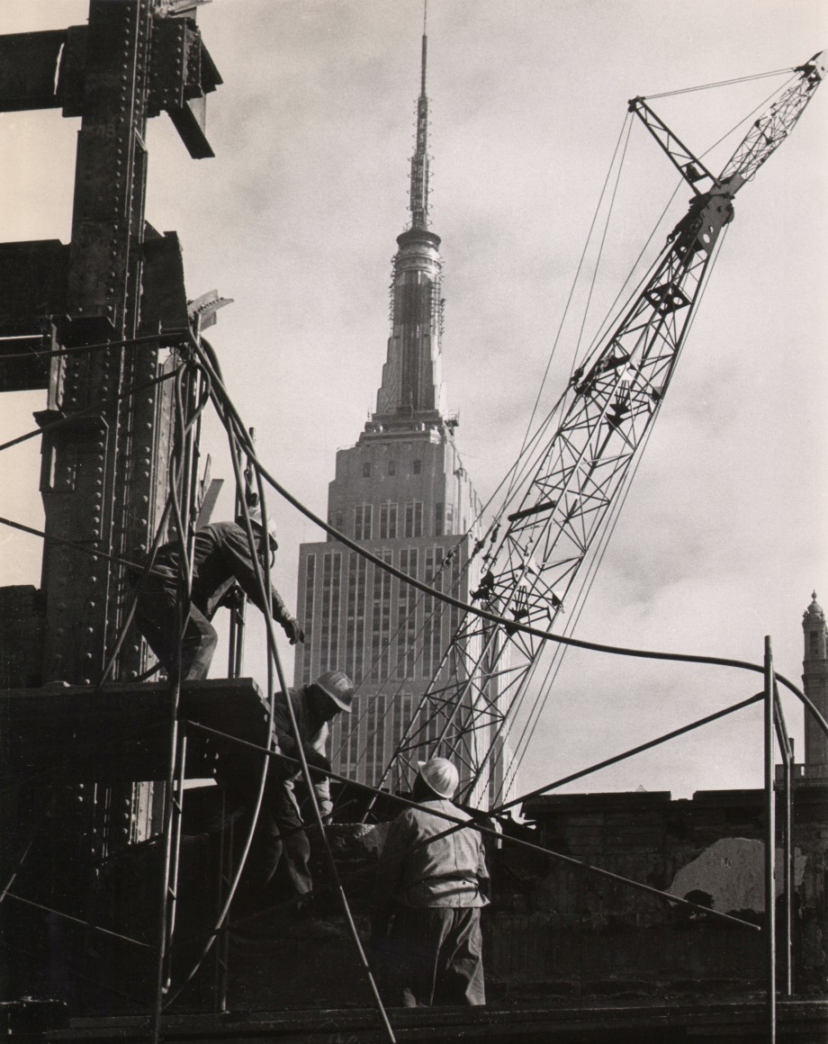 13. UPI Photo, Demolishing remains of Pennsylvania Station, ​1966. Workmen in the foreground amongst metal support structures and a crane. The top half of the Empire State Building is visible in the center background against a cloudy sky.