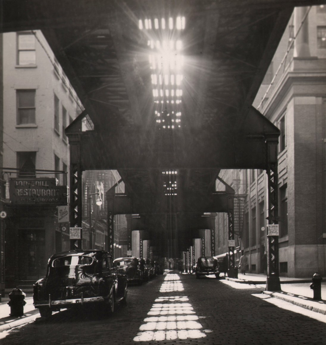 36. Fritz Neugass, The Sun Breaks Through, ​c. 1948. Street view beneath elevated train tracks with dramatic light and shadow.