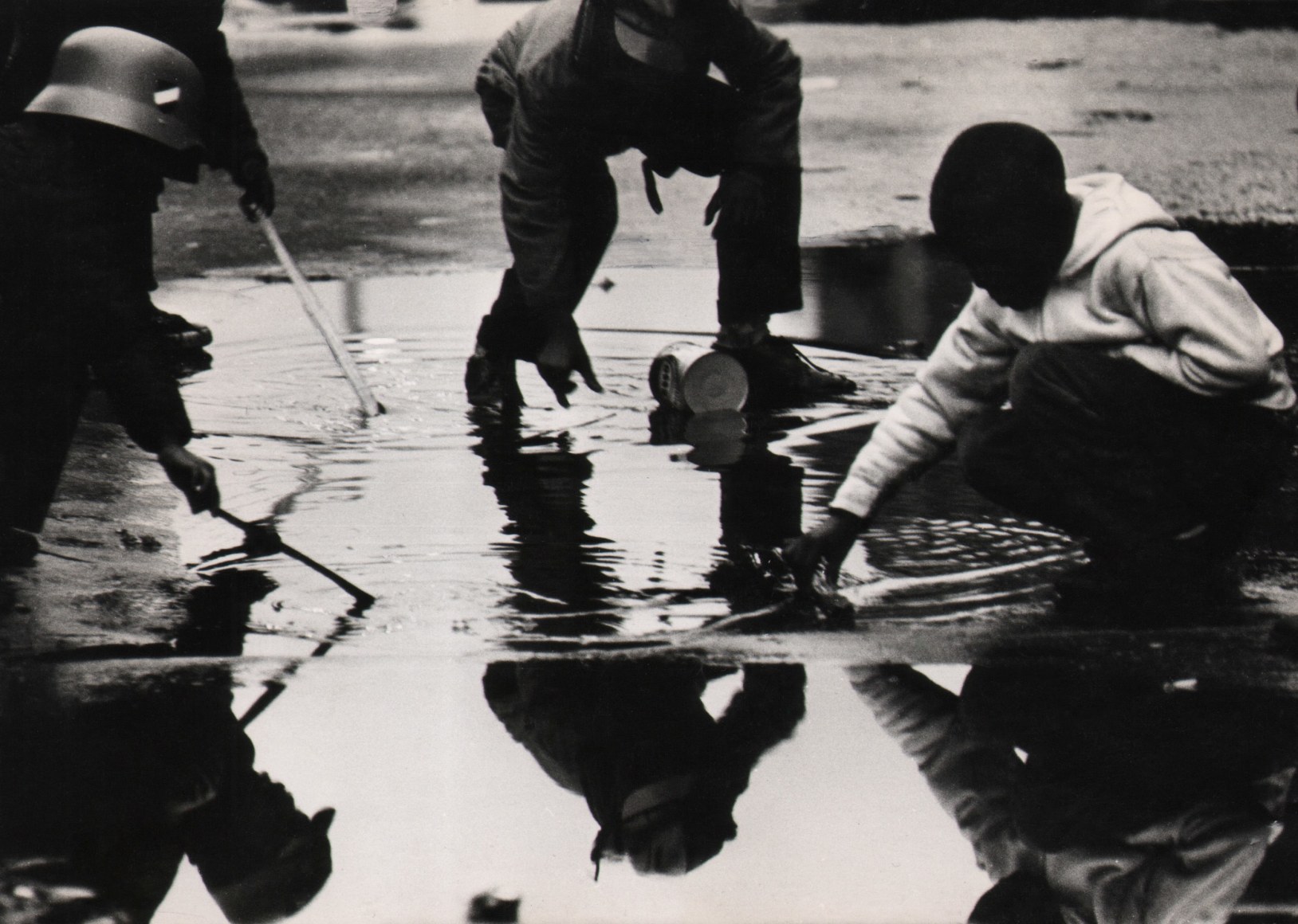 39. Beuford Smith, Reflection #1, Harlem, ​1965. Figures crouched, reaching into a large puddle on the street.