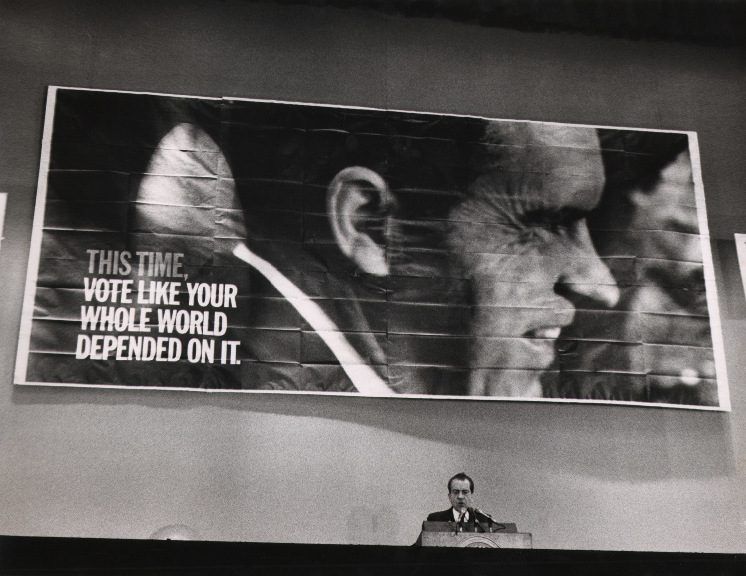 33. Howard Sochurek, Richard Nixon Campaign, ​1968. Nixon stands at a podium at the bottom of the frame. Above him, a large banner with his photograph reads &quot;This time, vote like your whole world depended on it&quot;