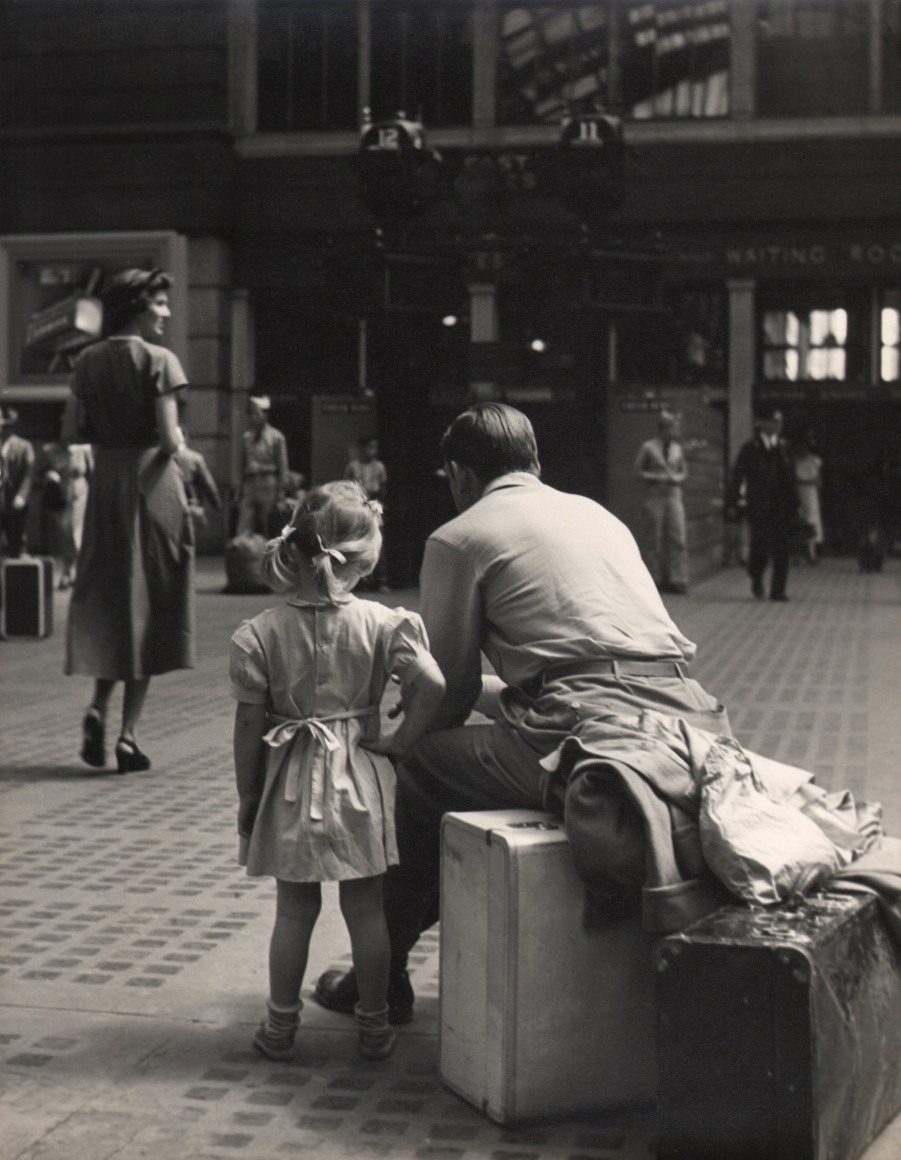 07. Simpson Kalisher, Untitled (Penn Station), ​c. 1949. Rear view of a young girl standing beside a man sitting on a suitcase.