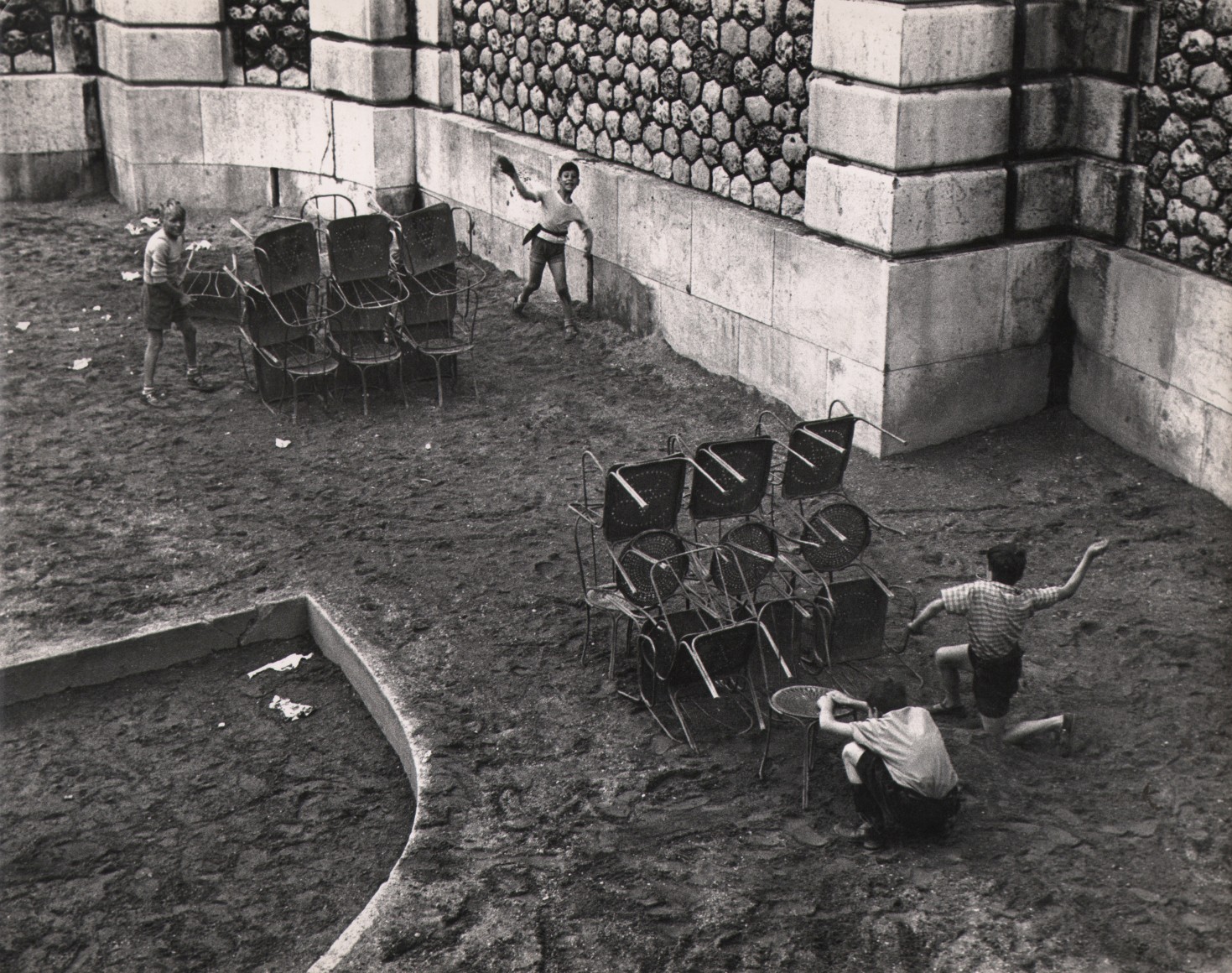 44. Sabine Weiss, La guerre aux pied du &quot;Sacre Coeur,&quot; Paris, c. 1950. Four young boys play war on a lawn, with to barricades made of stacked chairs.