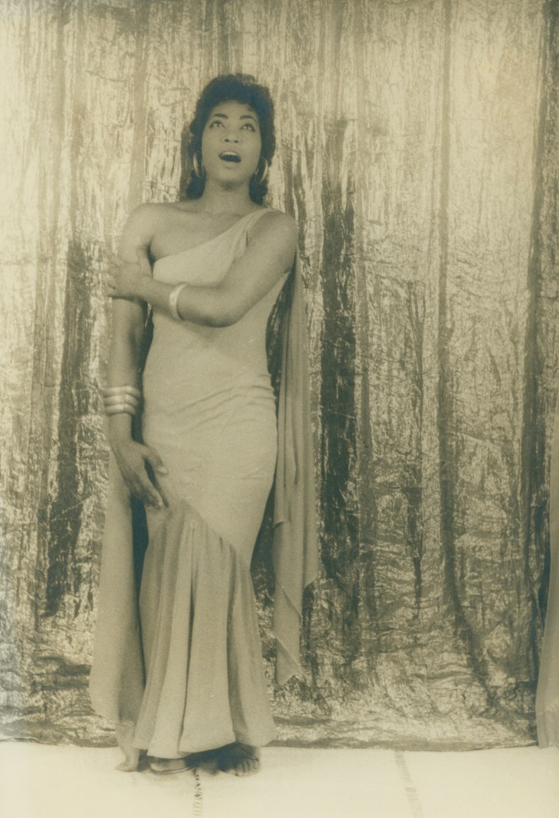 12. Carl Van Vechten, Gloria Davy as Aida, 1958. Full-body portrait with subject in an asymmetrical gown against a textured curtain backdrop, eyes cast up and mouth open in song.