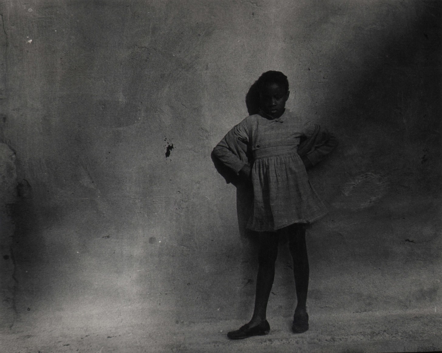 19. Beuford Smith, Little Girl in Park, ​1968. Dark exposure of a young girl standing against a concrete wall with hands on her hips.