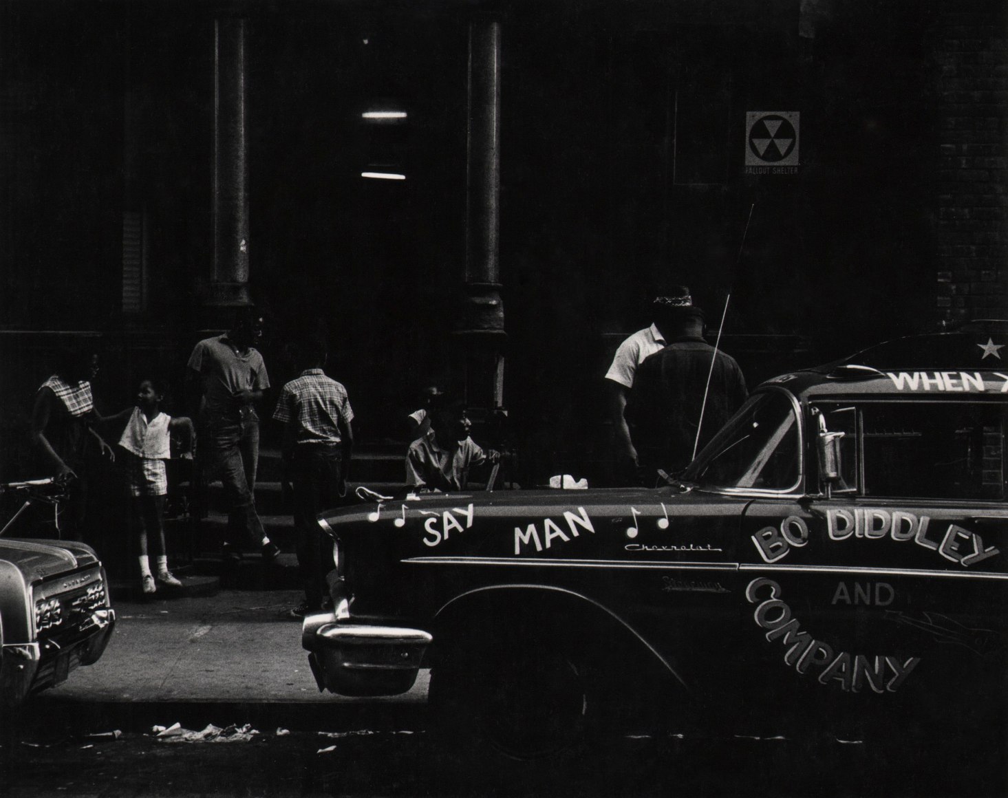 27. Beuford Smith, Say Man, Harlem, ​1969. A car parked on the street that reads &quot;Say Man&quot; and &quot;Bo Diddley and Company&quot;. Figures gathered on the sidewalk behind.
