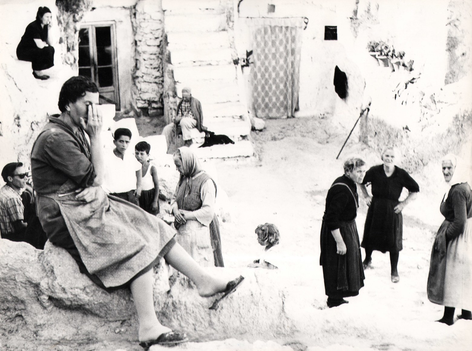 Mario Giacomelli, Puglia, ​1958/1970. High-contrast street scene with various people sitting and standing in groups.