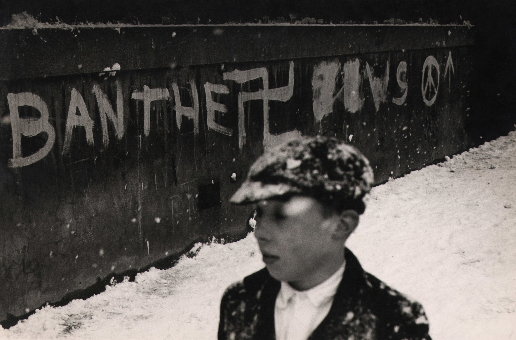 40. Donald McCullin, A bleak scene which expresses a bleak mood, from Finsbury Park, c. 1966. A young man in the foreground walks through the snow; the wall behind him reads &quot;ban the Jews&quot; in graffiti.