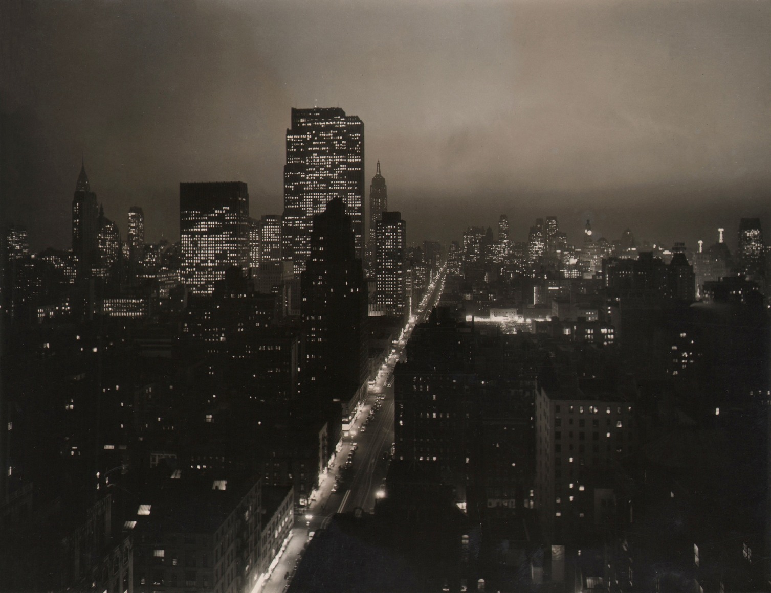 Paul J. Woolf, Sixth Avenue Looking South, ​c. 1935. Night time cityscape with an illuminated Sixth Avenue running diagonally up and right in the center of the frame.