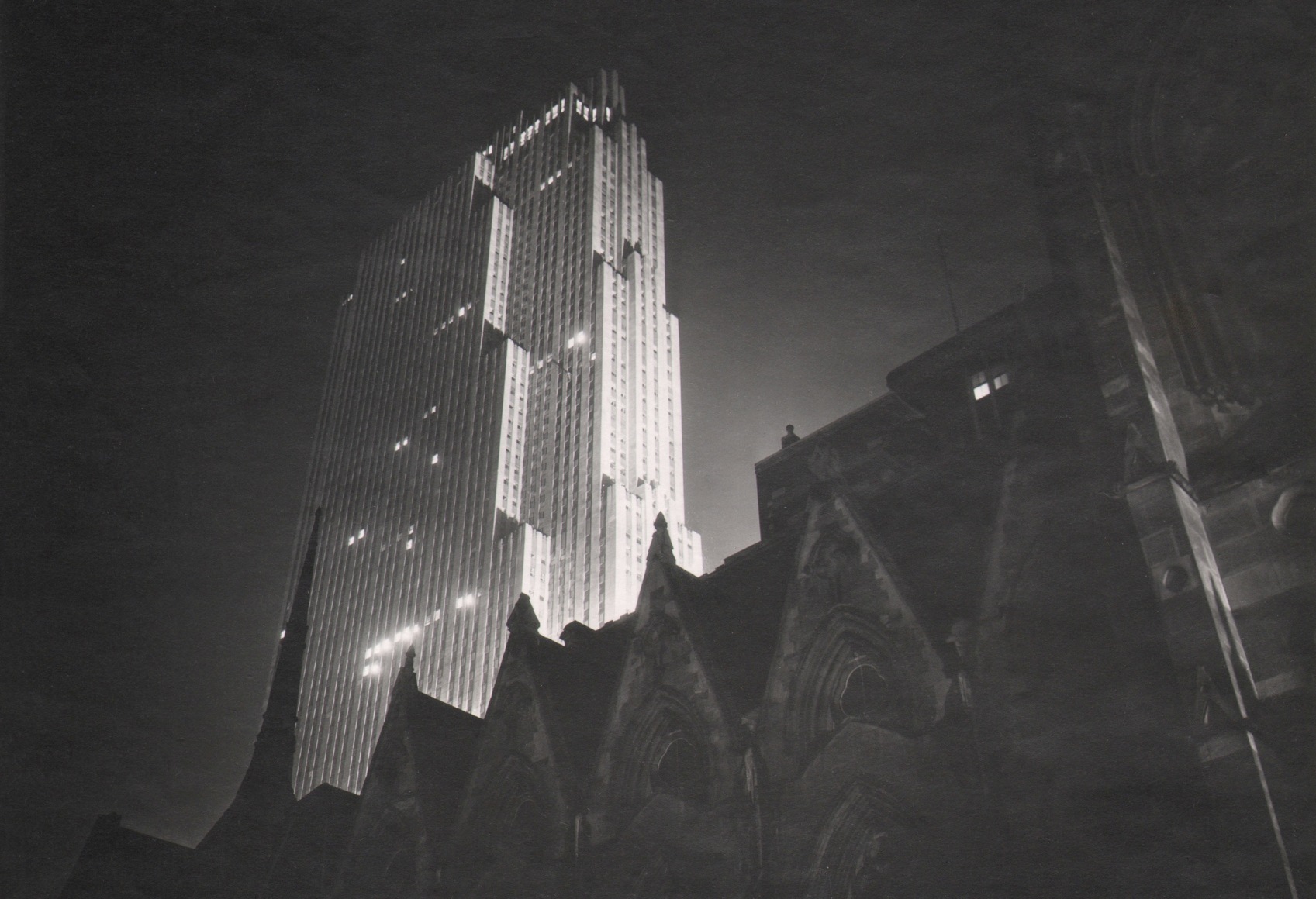 Paul J. Woolf, RCA Building at Night, ​c. 1936. Silhouetted cathedral in the foreground against the tall RCA Building rising up on the center left of the frame.