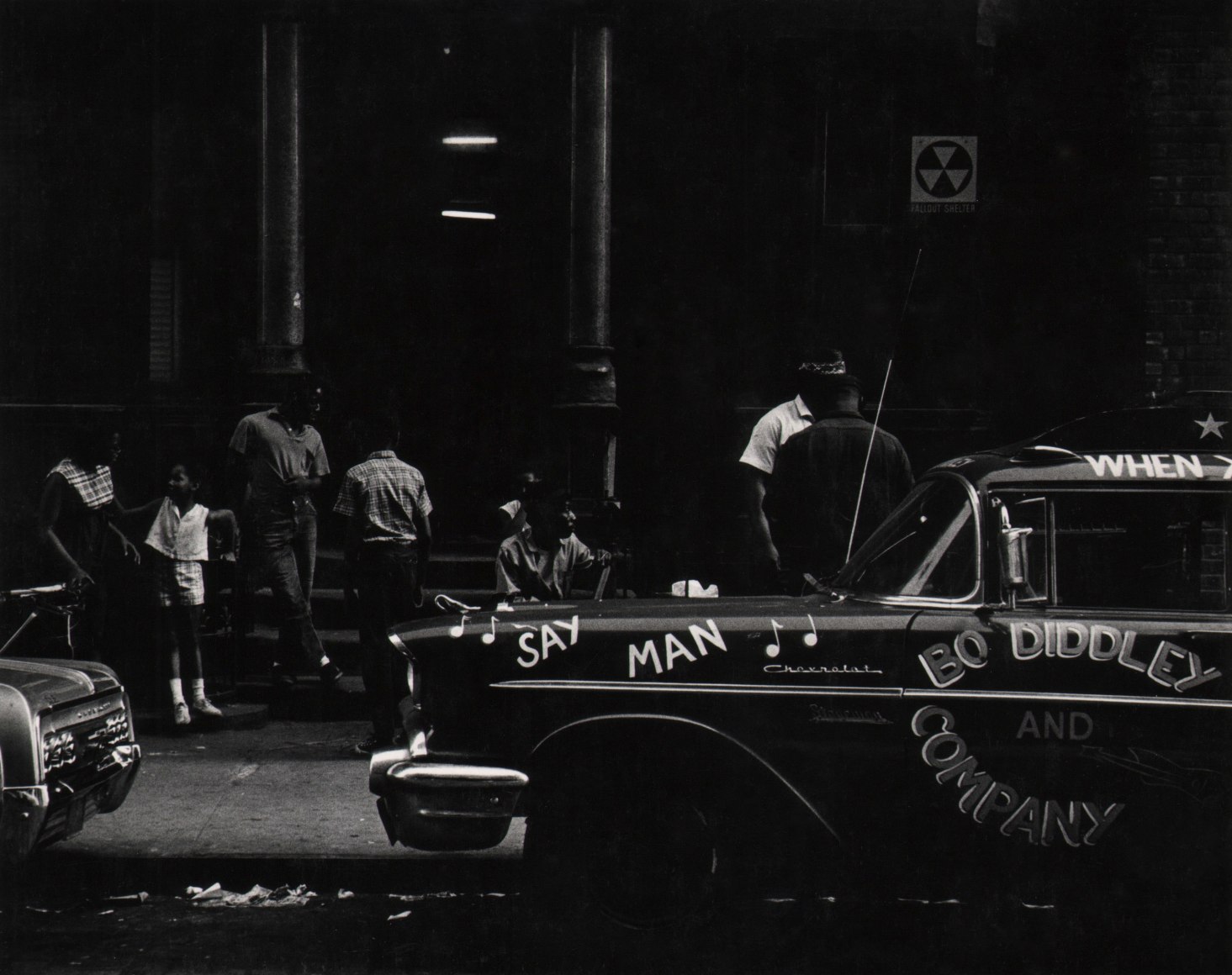 30. Beuford Smith, Say Man, Harlem, ​1969. A car parked on the street that reads &quot;Say Man&quot; and &quot;Bo Diddley and Company&quot;. Figures gathered on the sidewalk behind.