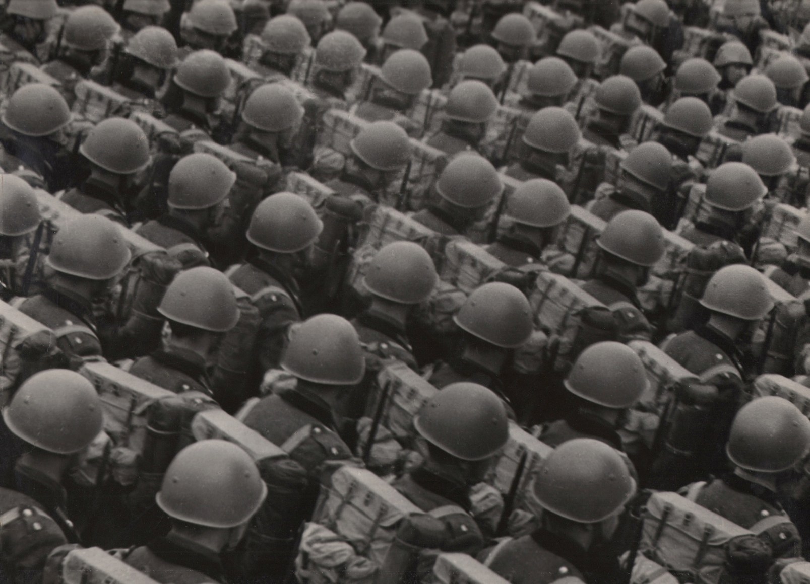 Italo Bertoglio, Le case di fronte, c. 1937. Diagonally composed rows of soldiers in helmets photographed from behind.