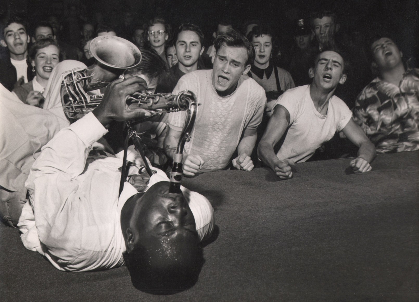 Bob Willoughby, Big Jay McNeely, ​1951. Subject lays on stage mid-performance, playing the saxophone while emotional fans look on.