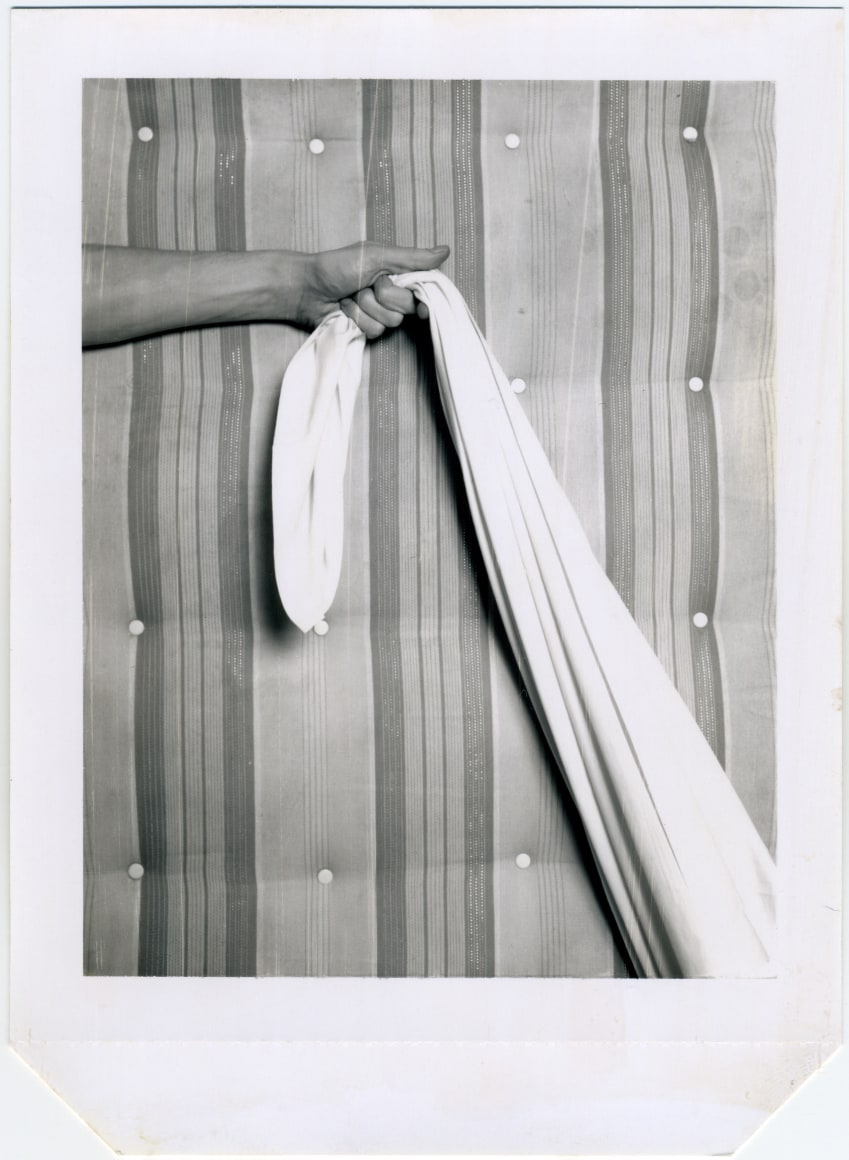 Hand holding sheet, mattress as background.