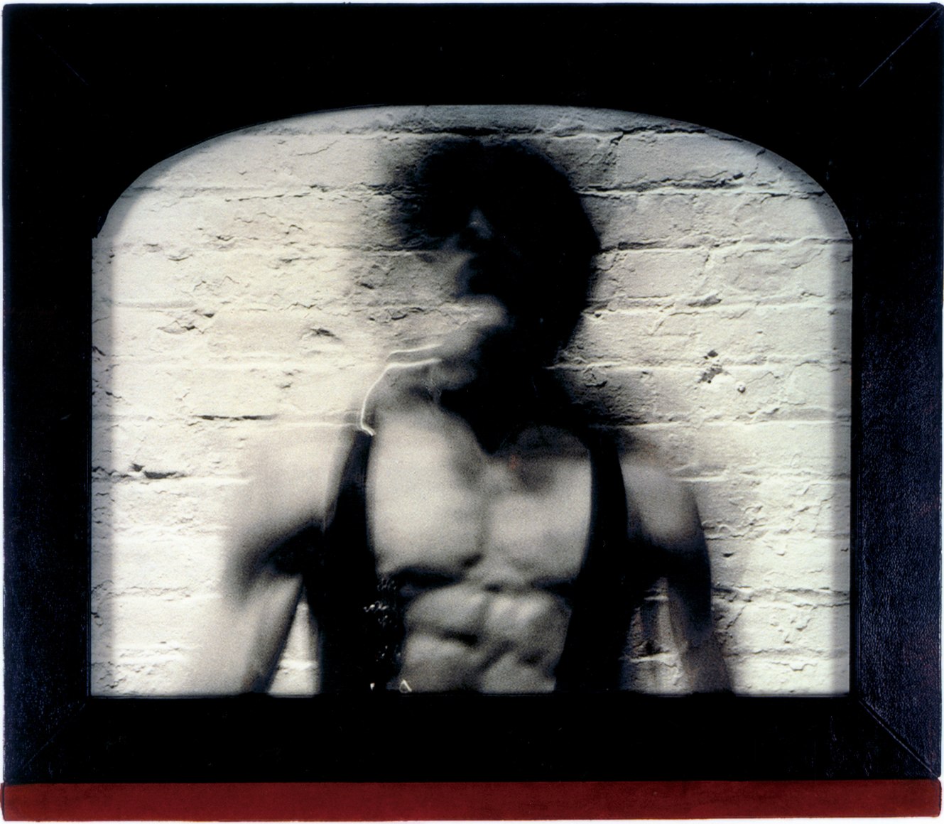 Self portrait in open vest against brick wall