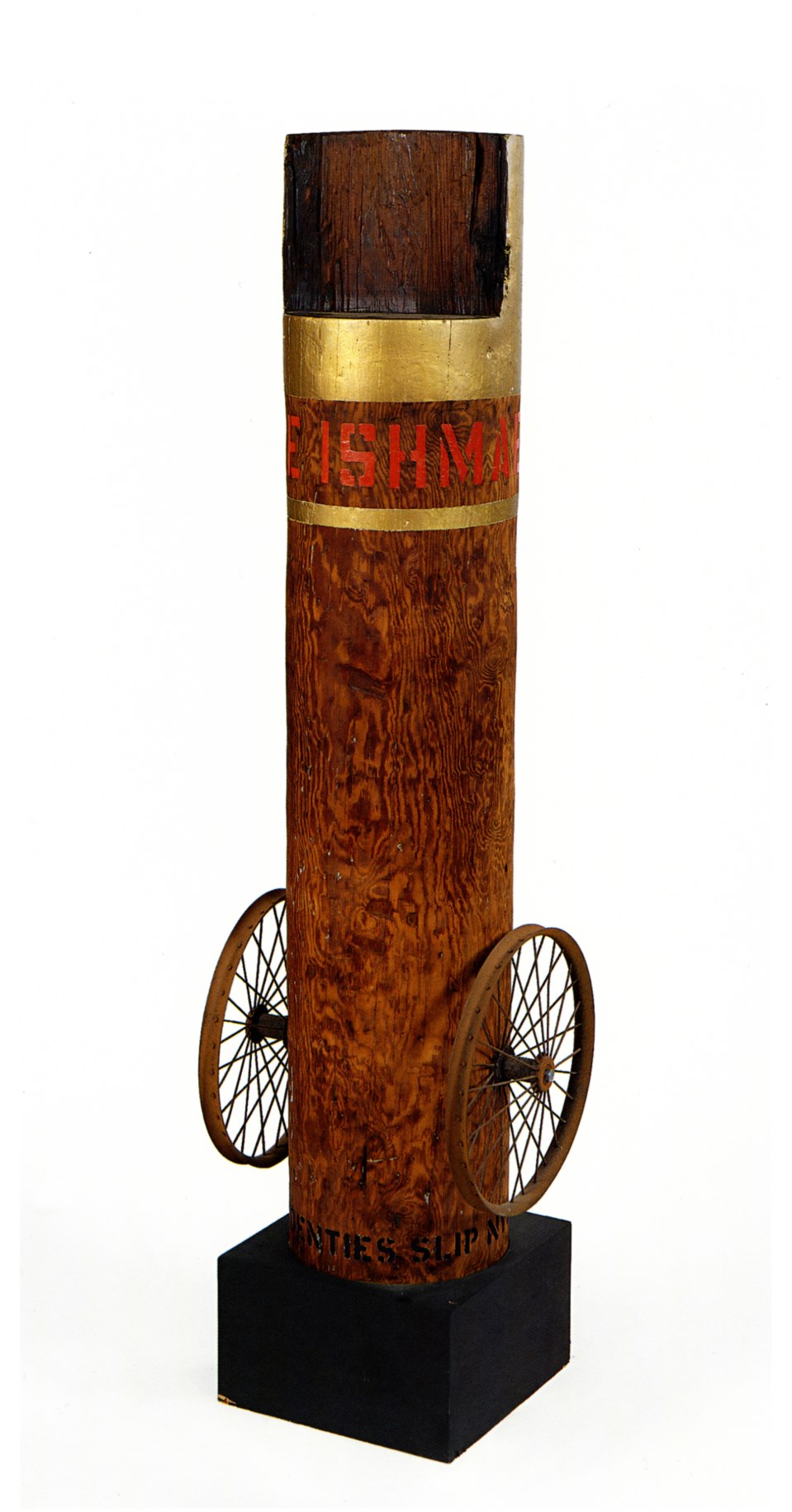 A 62 3/4 by 17 by 14 inch column with an iron wheel affixed on the bottom right and left sides, and standing on a wooden base. The top of the column is painted gold. Below, wrapping around the column, is the work's title, &quot;Call Me Ishmael,&quot; painted in red letters. Below the text a thin gold stripe wraps around the column.