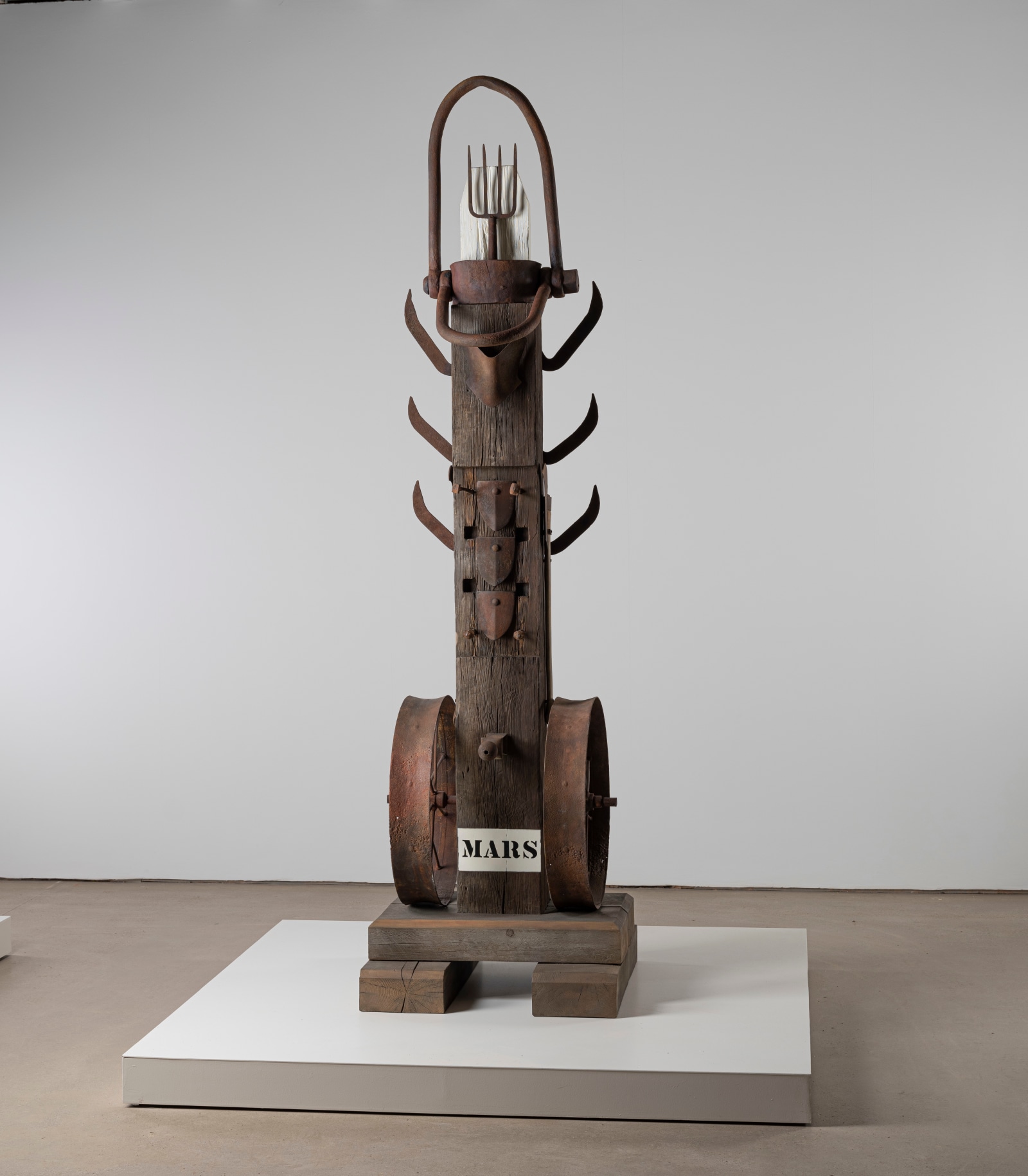 A 131 5/8 by 35 7/8 by 35 7/8 inch painted bronze sculpture consisting of a beam atop a base. The work's title, &quot;Mars,&quot; appears in stenciled letters against a white ground across the front bottom of the sculpture. A wheel is affixed to both the bottom right and left sides of the sculpture. Three brush axes have been affixed to both the upper right and upper left sides of, and a pitchfork has been affixed at the top of the sculpture.