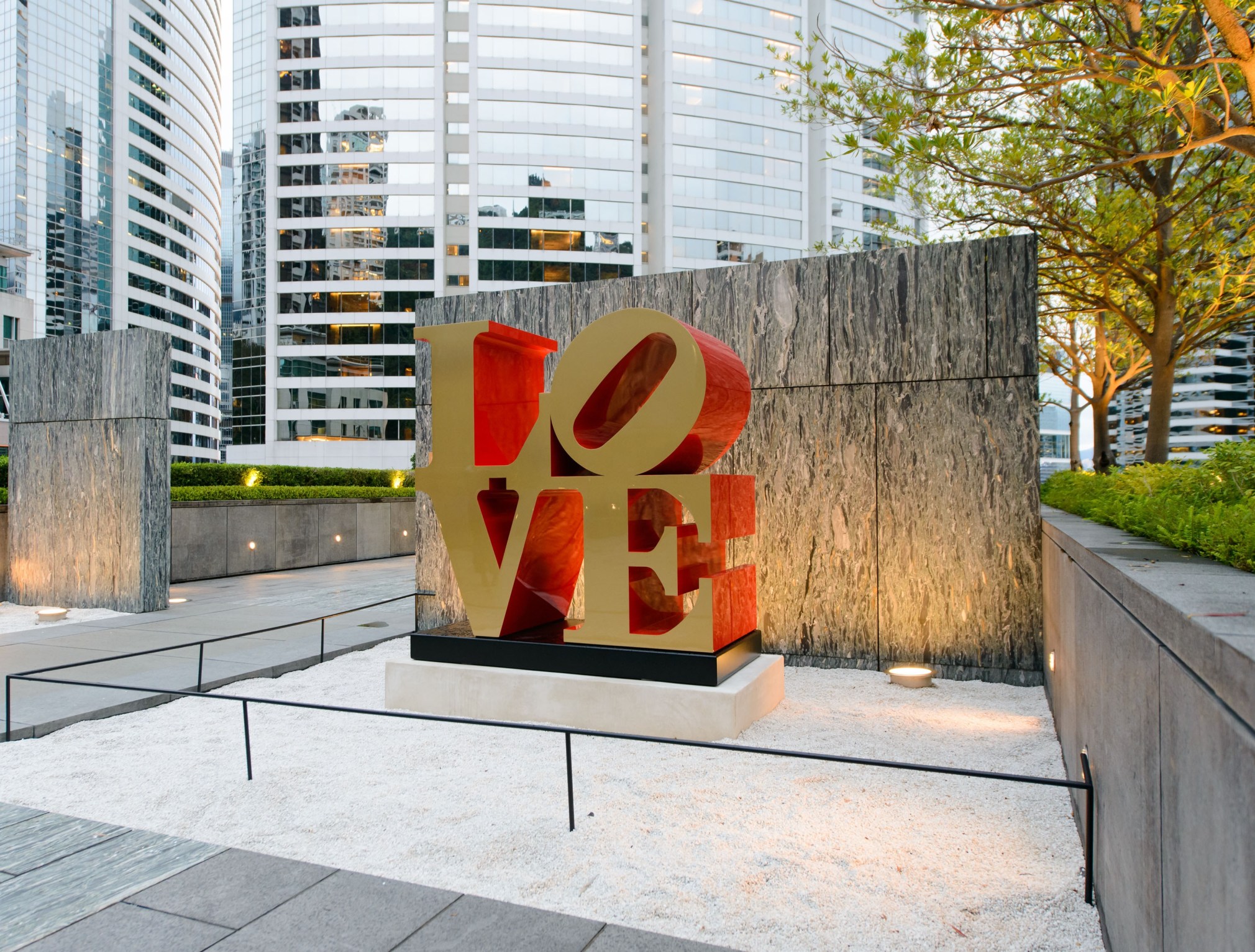 A 72 by 72 by 36 inch polychrome aluminum sculpture spelling love, consisting the letters L and a tilted letter O on top of the letters V and E. The faces of the letters are gold, and the sides are red.