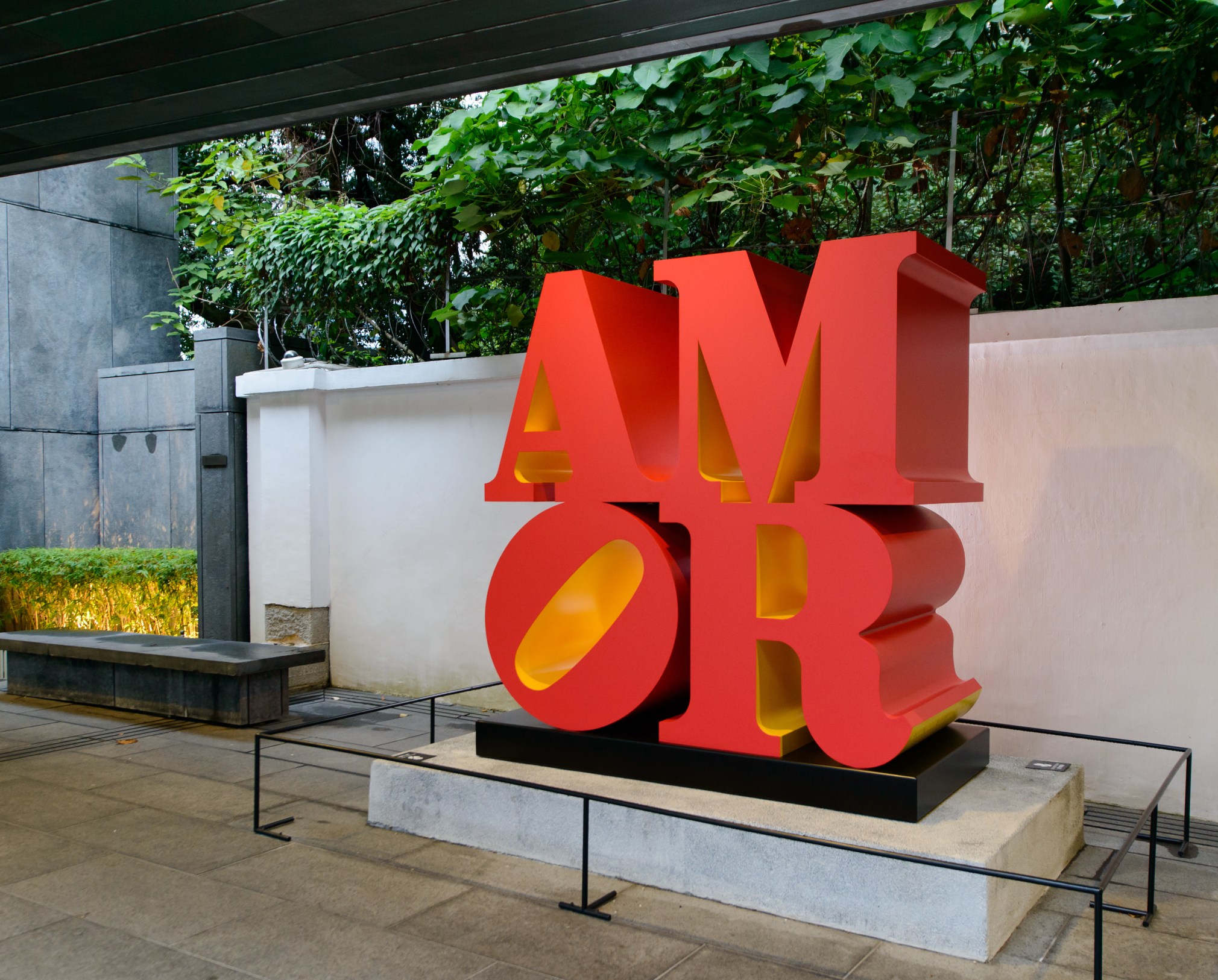 AMOR, a 72 by 72 by 36 inch polychrome aluminum sculpture consisting of the letters A and M atop a tilted O and R. The front, back and sides of the letters are red, and the insides are yellow.