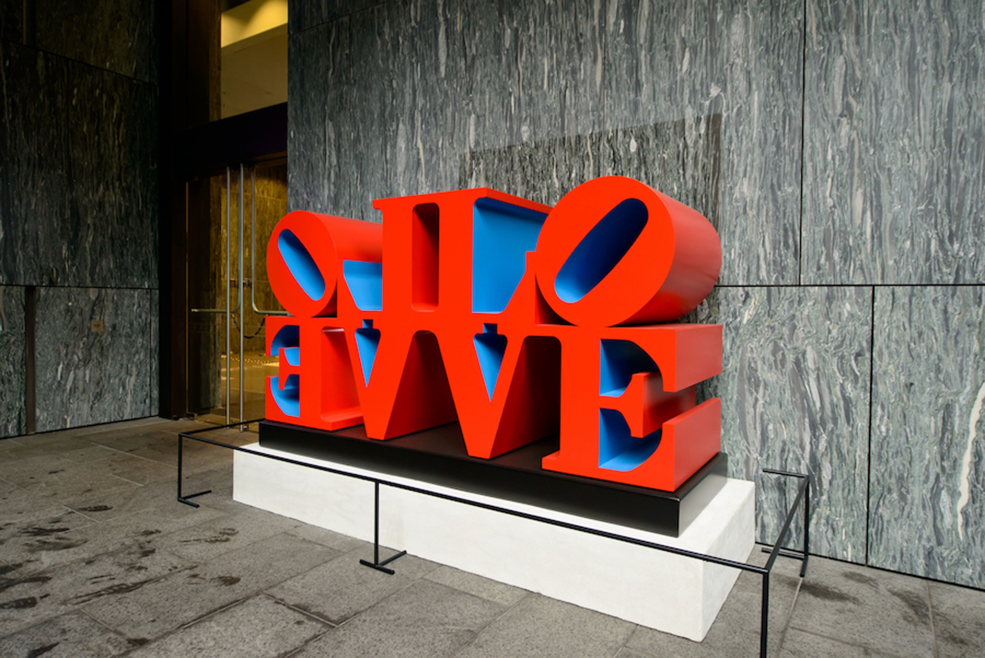 Imperial LOVE, a polychrome aluminum sculpture consisting of two quadripartite LOVE sculptures side by side, with the L and V of each sculpture back to back and the O and E facing outwards. The faces and sides of the sculpture are red, and the insides are blue.