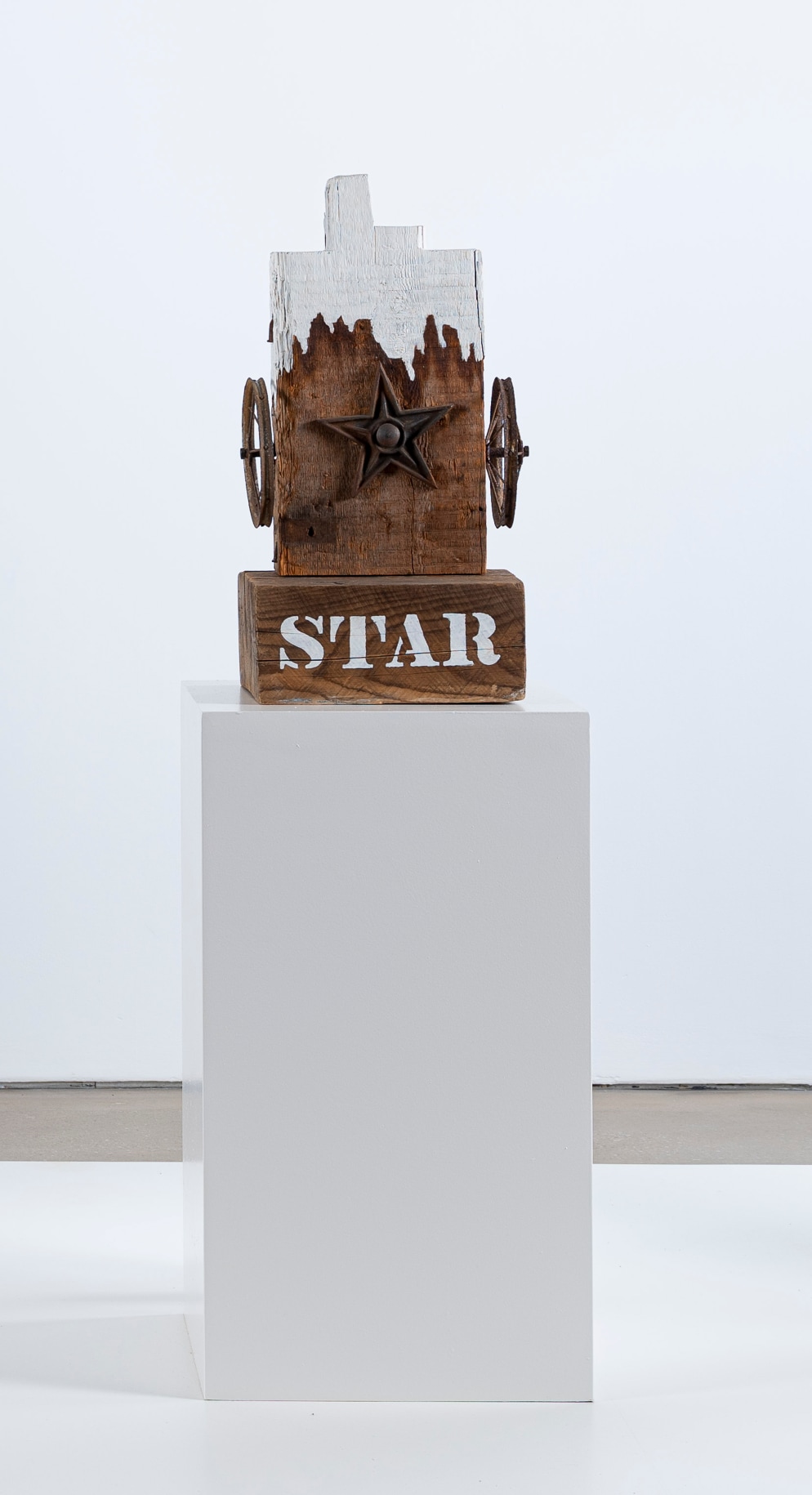 A 25 1/2 by 12 1/2 by 11 3/4 inch sculpture consisting of fragment of a wooden beam with a haunched tenon, resting on a wooden base. The work's title, &quot;Star,&quot; is painted in white stenciled letters across the front of the base. A metal star is affixed to the center front of the sculpture, and a small wheel has been affixed on both sides of the sculpture, to the left and right of the star. The top part of the sculpture has been painted white, with an uneven bottom edge, resembling dripping paint.