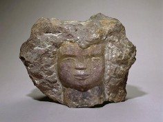 Stone sculpture. A simple face is carved into the rough, gray stone.