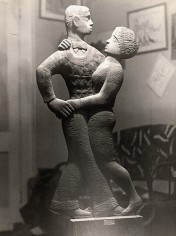 Black and white photo of a wood sculpture depicting two dancers. The sculpture is of a man and a woman closely ballroom dancing together. The sculpture depicts the side profile of each figure.