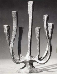 Black and white photo of a simple menorah, with the candle holders made long and stem-like.