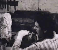 Film still of a man in a vertically striped shirt (Chaim Gross) with his back to the viewer, carving a sculpture depicted at left.
