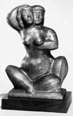 Black and white photo of a sculpture of two people seated, embracing each other while facing us. Their bodies are interconnected, with a female form being majority visible while the form behind her is hidden. She reaches up to caress the other figures head while their hand is melded into her chest.