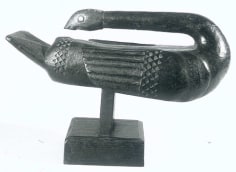 Polished wooden sculpture of an elongated bird positioned on a small square base. The body of the bird is rectangular in shape, with its exaggeratedly long neck stretching backward above the body of the bird, until its head reaches its tail. Triangular motif carved in relief on wings and body.