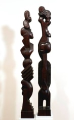 Two dark wooden sculptures. The sculptures are tall and thin, composed of stacked geometric forms.