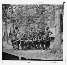 Two young Black men stand behind a group of seated white officers, Camp of the 93rd New York Infantry, Bealton, VA, August, 1863 (Courtesy of Library of Congress)