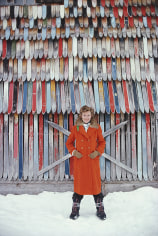 Slim Aarons, Princess Ruspoli, 1979: Princess Lucy Ruspoli stands in front of a colorful wall of old skis in Lech am Arlberg, Austria
