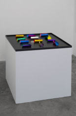 A sculpture of 12 pieces of paper on a black stage, on a white pedestal