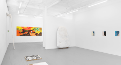 A wide photograph of the gallery. Starting at right: three enamel paintings on steel, one large sculpture leaning against the temporary wall in the gallery, one large horizontal painting on the back wall, one small illegible painting on the left wall with a large sculpture next to it, and one print installed on the ground at left.