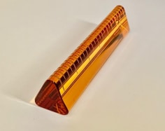 An orange, hand-blown glass sculpture that looks like a ruler. It is triangular, 6 inches long