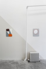 A photograph of 2 enamel paintings, one on a gray wall, one on a white wall. A diagonal separates the 2 and defines the space.