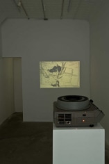 A photograph of the projector throwing an image onto the back wall. The projector is on a white pedestal