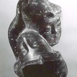 Metal sculpture of two intertwined female heads with serene expressions on their faces. Both of the heads have specks of white dots on them. 