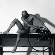Nude black man sitting and looking downward.