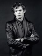 Man wearing a leather jacket stands with arms folded.